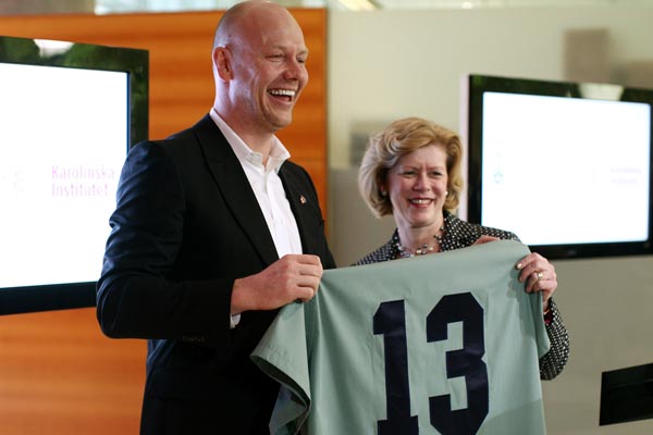 Former Toronto Maple Leafs captain Mats Sundin beams as he and Dean Cathy Whiteside display the U of T Faculty of Medicine&#039;s gift of medical scrubs bearing his iconic No. 13. (Photo by Dave Chan)